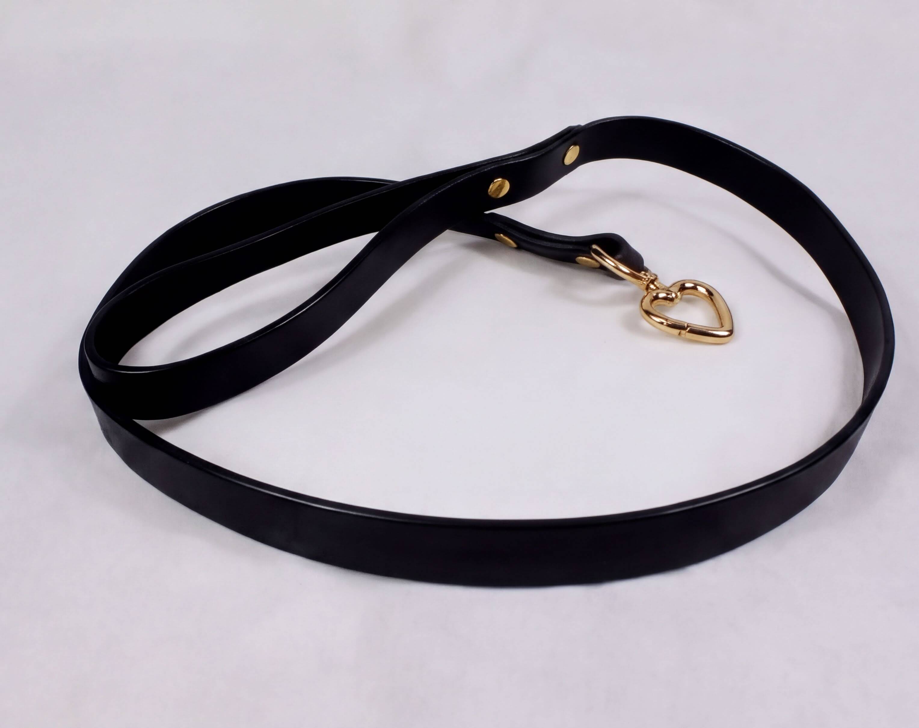 A black leather leash with a gold heart-shaped charm attached to it.
