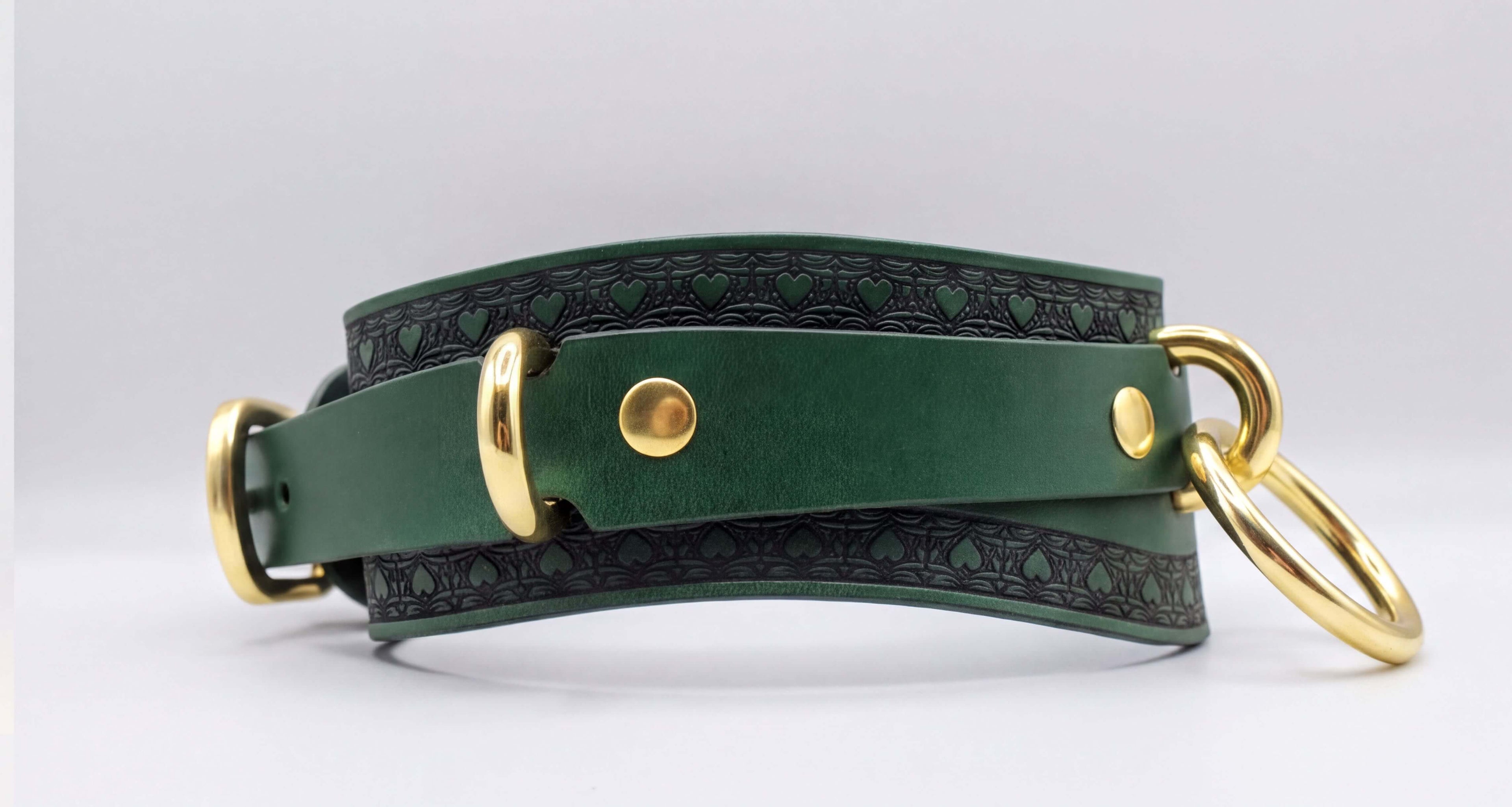 A green leather choker collar with gold hardware, including a buckle and two rings, is shown in the image.