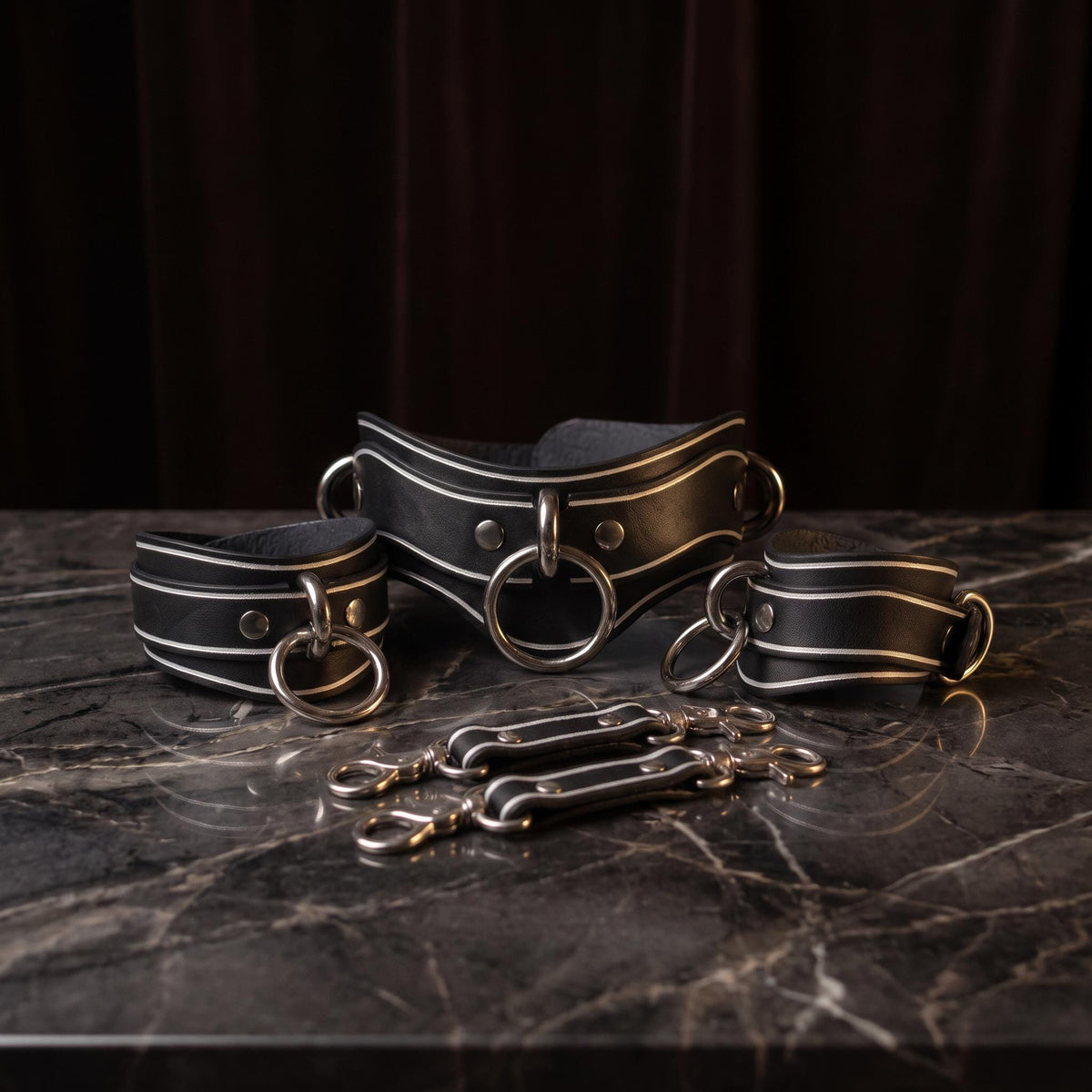 A set of black leather straps with metal rings and buckles, arranged on a marble surface.