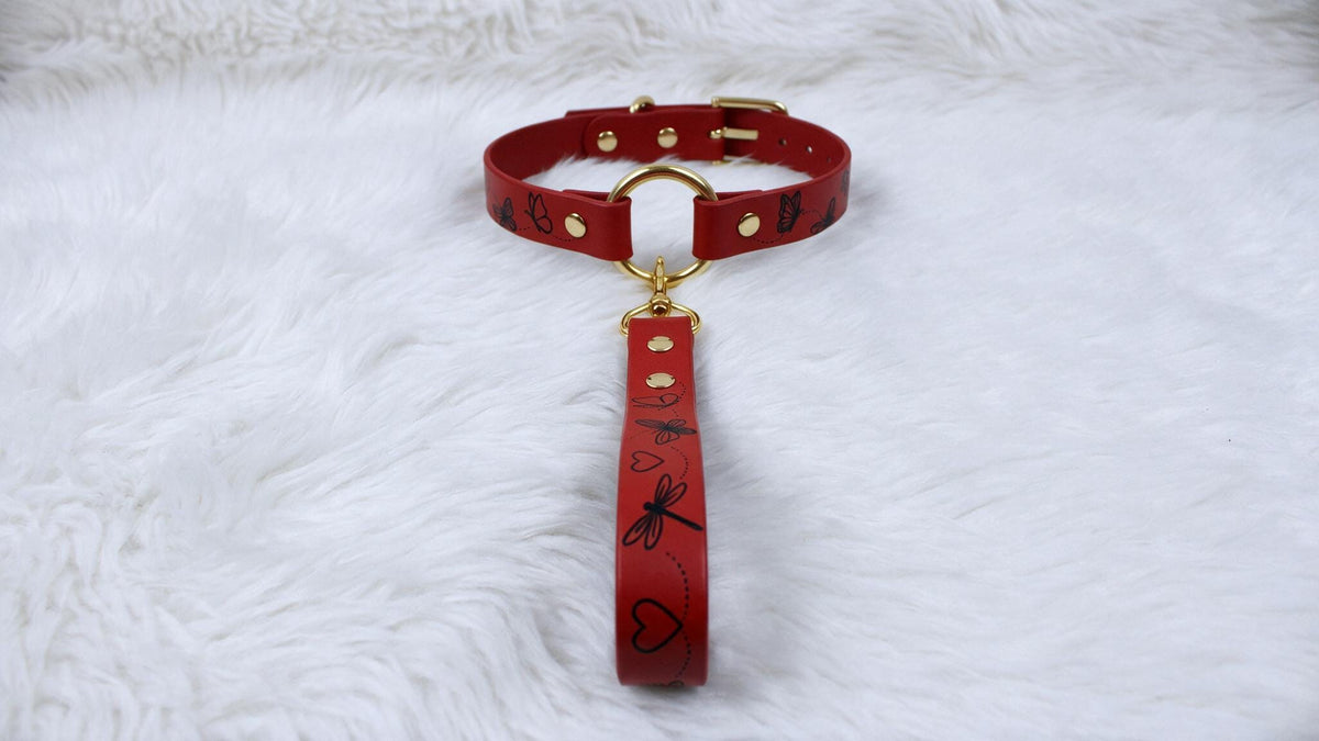 A red collar with a gold buckle and a red leash attached to it, placed on a white furry surface.