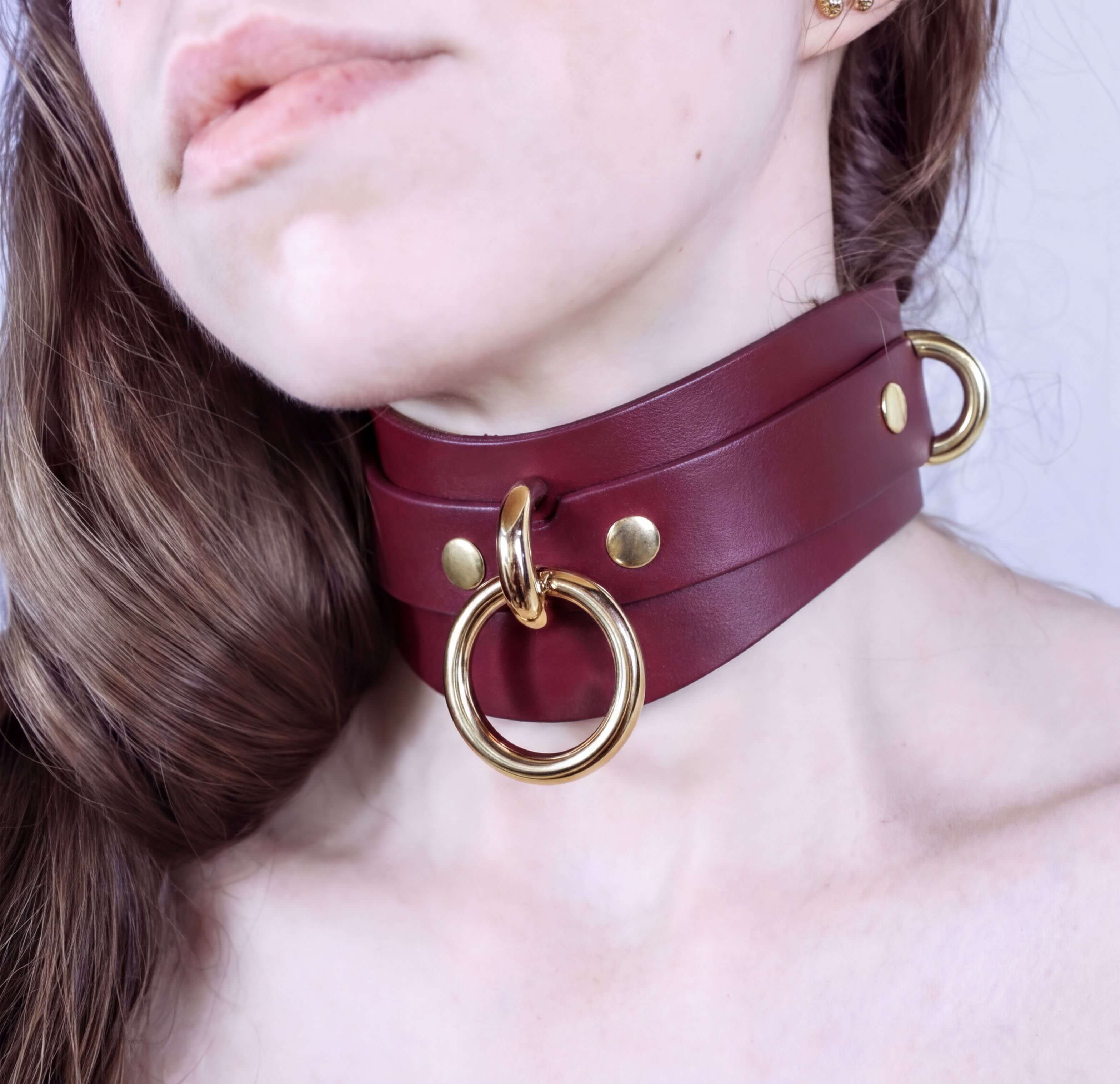 A close-up of a woman's neck wearing a burgundy leather choker necklace with gold-colored metal rings.