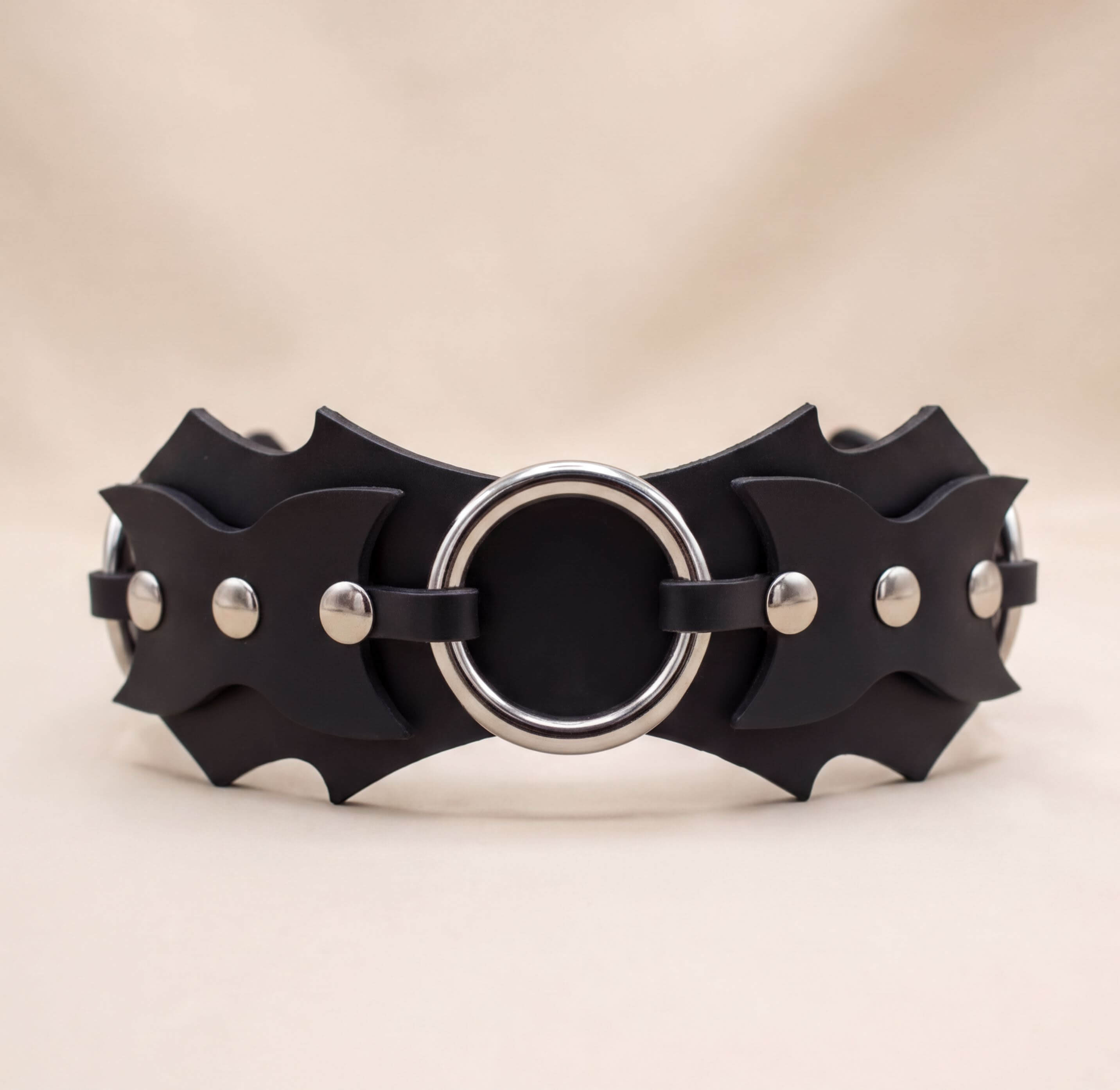 A black leather belt with a circular metal ring and three metal studs on the sides.
