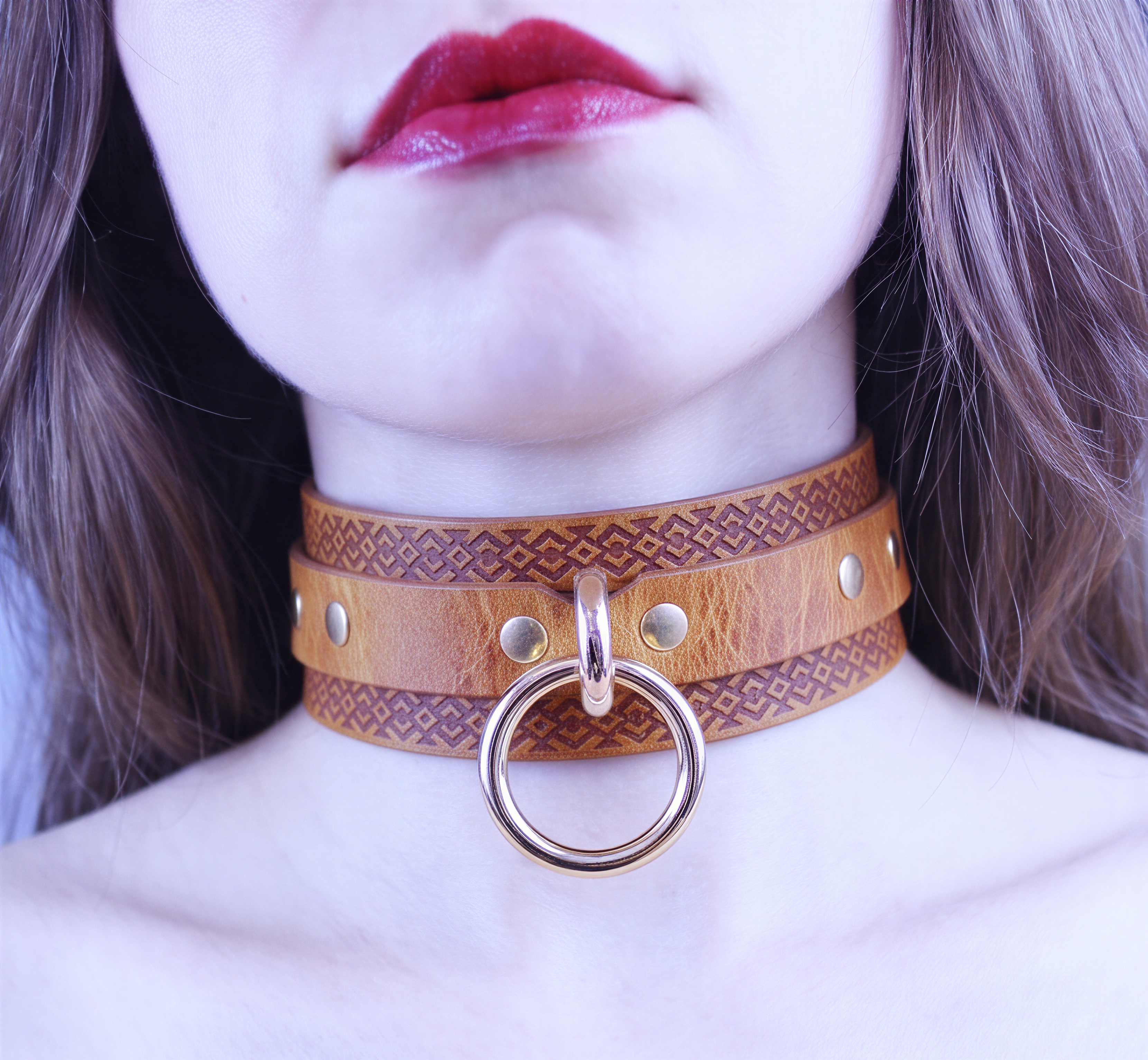A close-up of a woman's face wearing a leather choker necklace with a metal ring and studs.