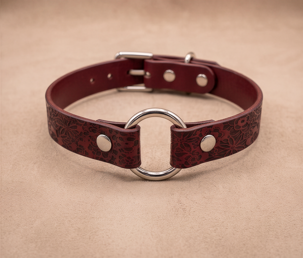 A burgundy leather collar with a metal ring and buckle, displayed on a beige background.