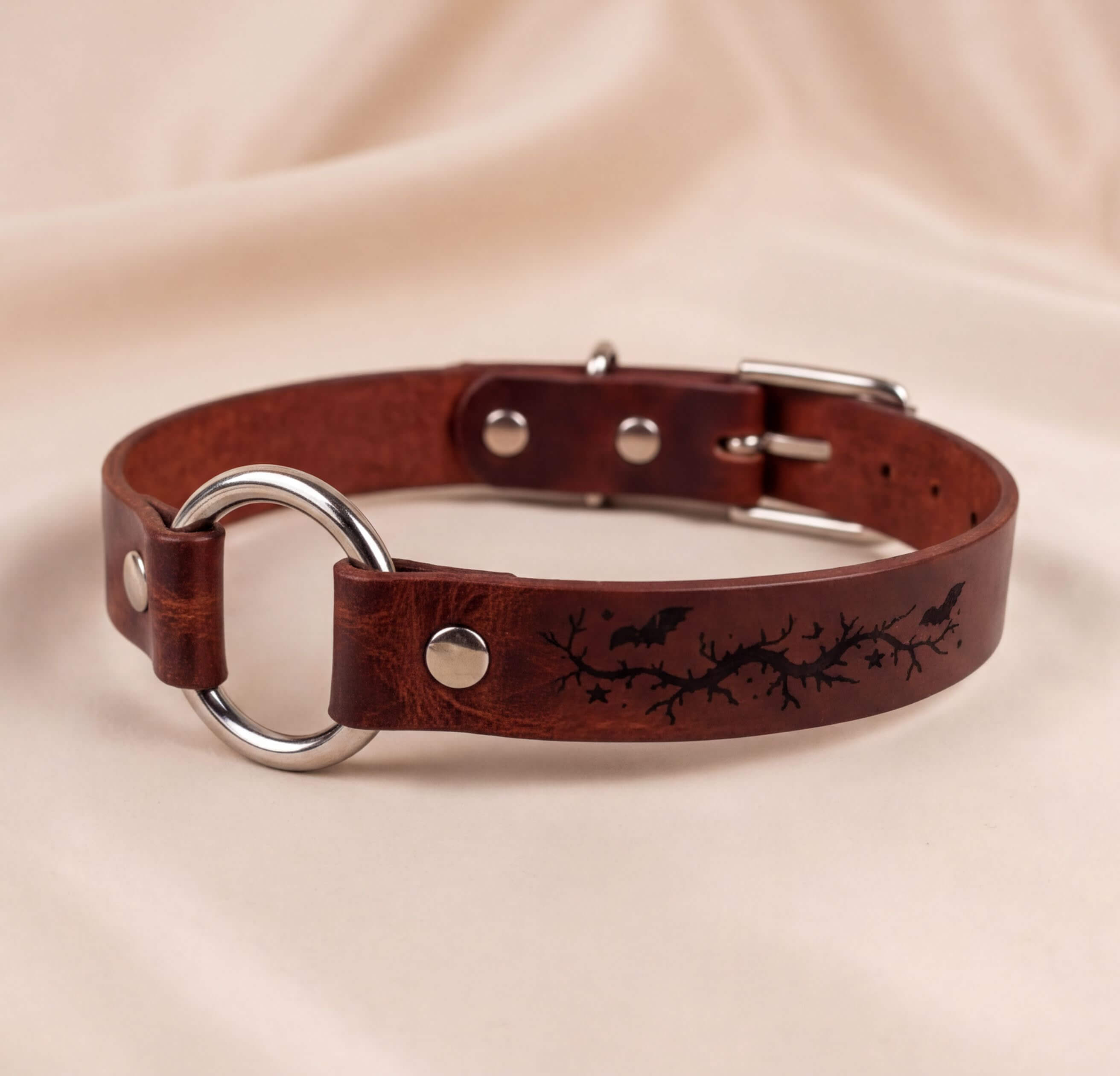 A brown leather collar with a metal ring and a design featuring bats and branches.