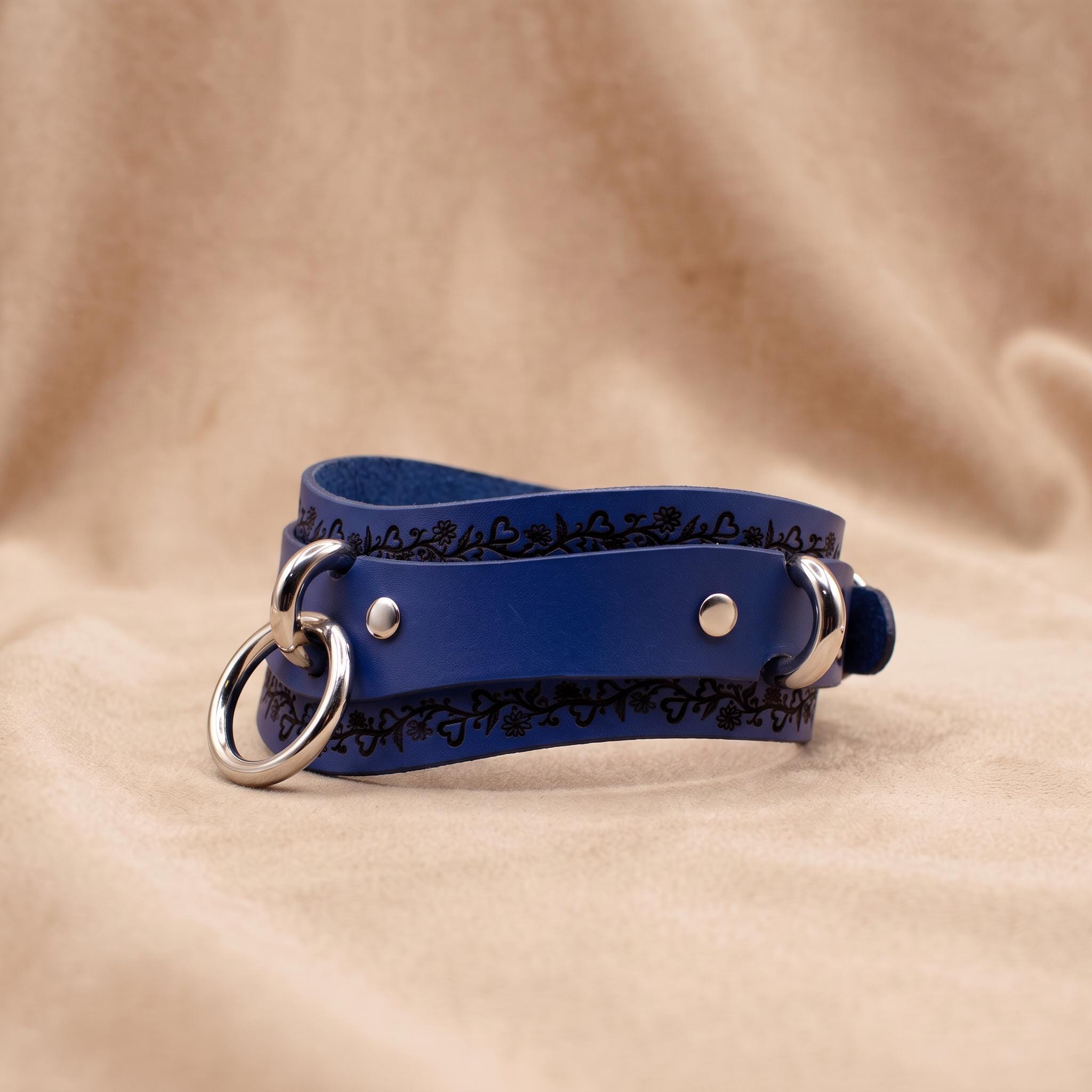 A blue leather choker necklace with metal rings and a decorative pattern on the clasp.