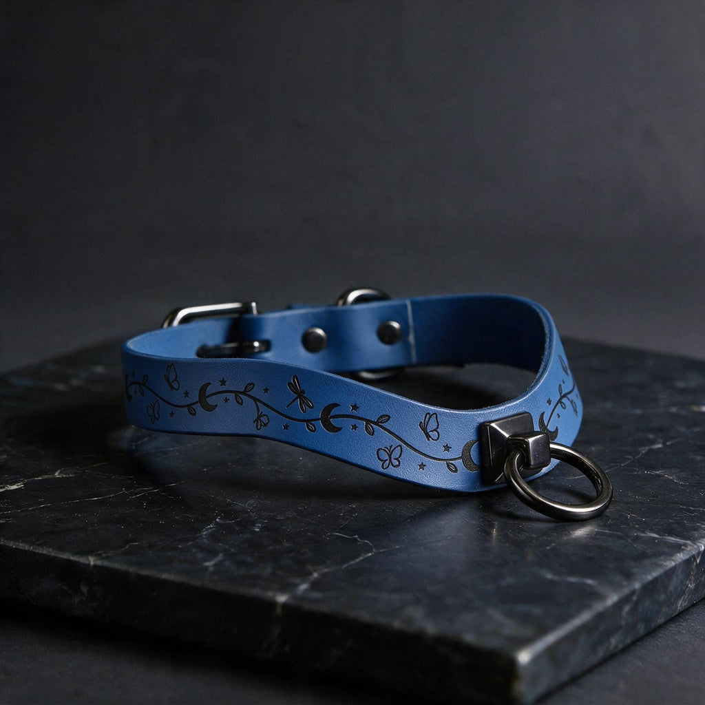 A blue leather collar with a metal ring and decorative elements rests on a dark surface.