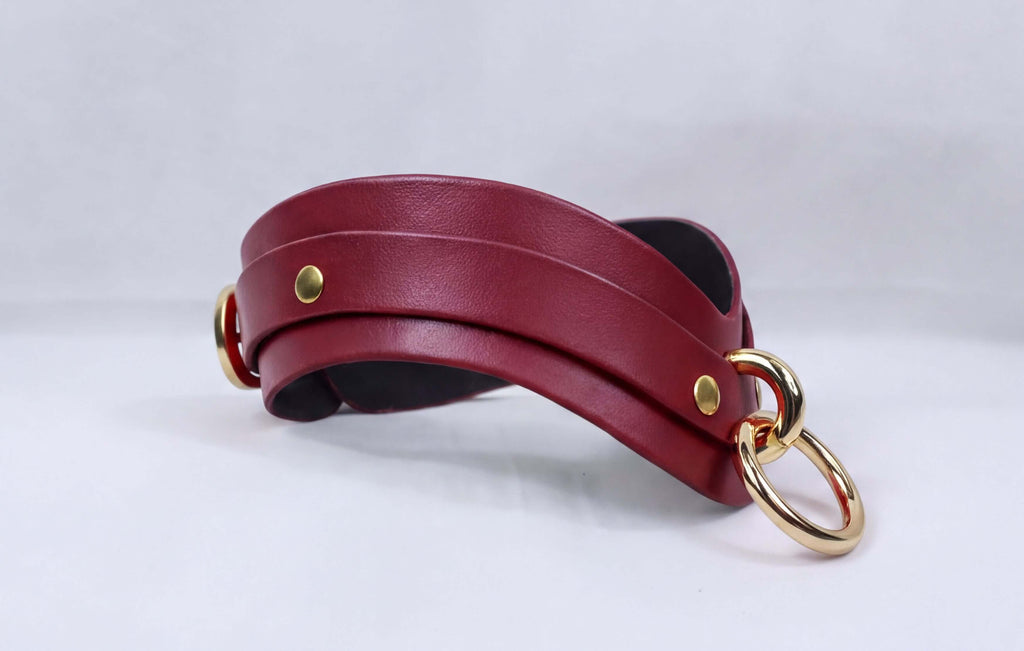 A burgundy leather choker necklace with gold-colored metal rings and a black interior.
