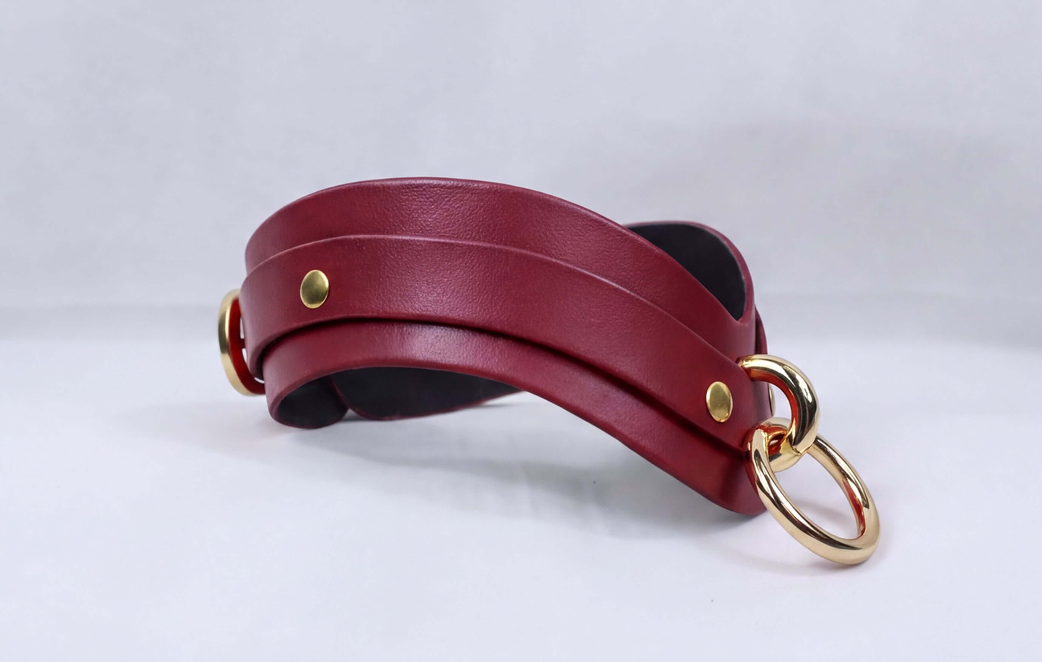 A burgundy leather choker necklace with gold-colored metal rings and a black interior.