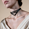 A close-up of a woman's neck and chest area, with a black choker necklace featuring a triangular design.