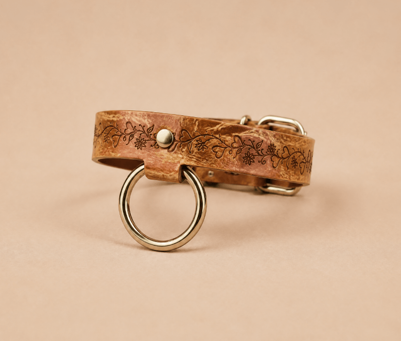 A brown leather collar with a metal ring and a floral design on it.