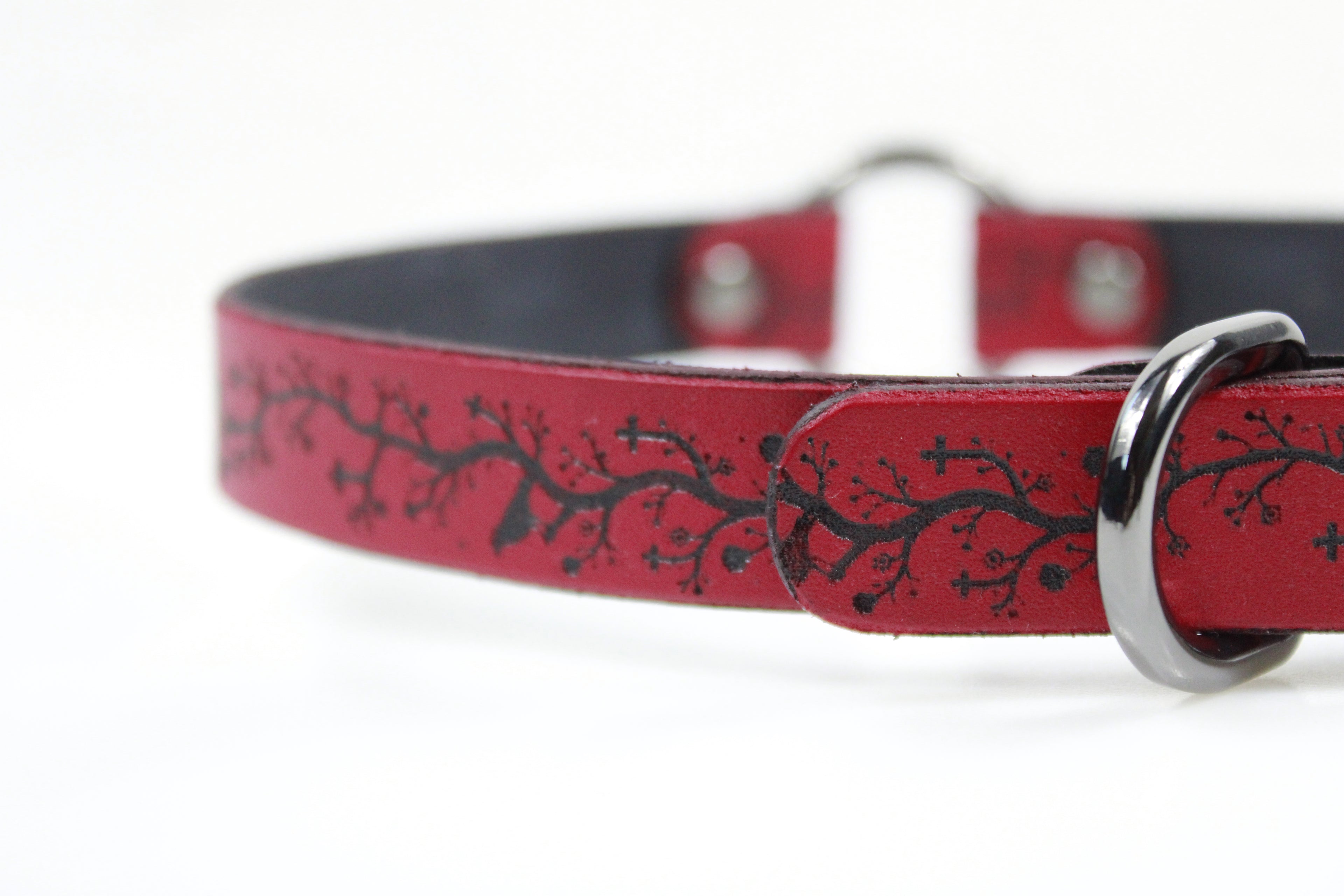 A close-up view of a red leather dog collar with a black tree branch design.