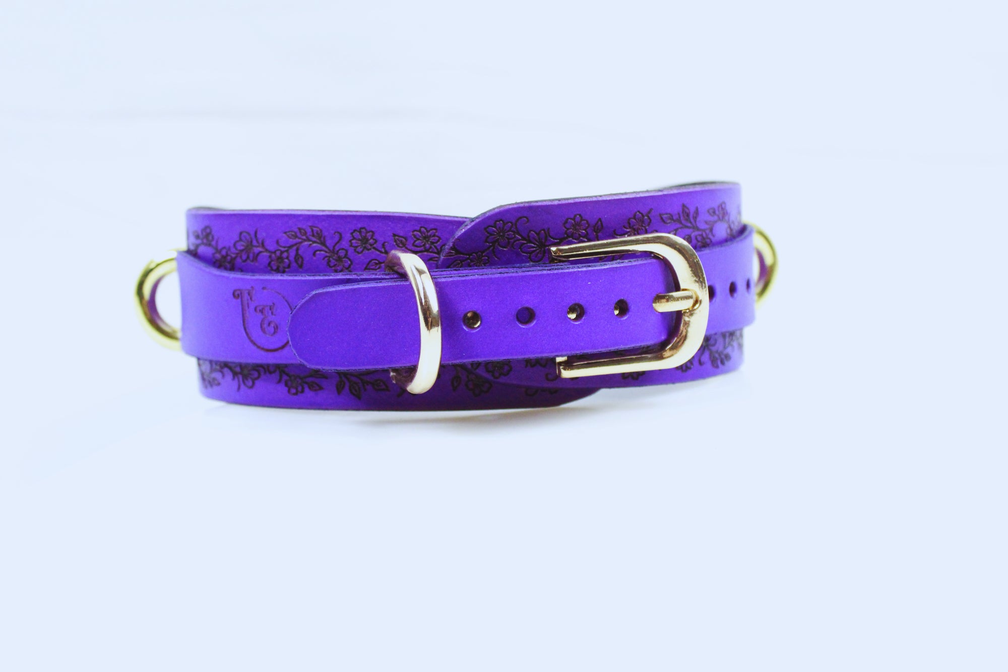 A purple leather belt with a floral pattern and a gold buckle.