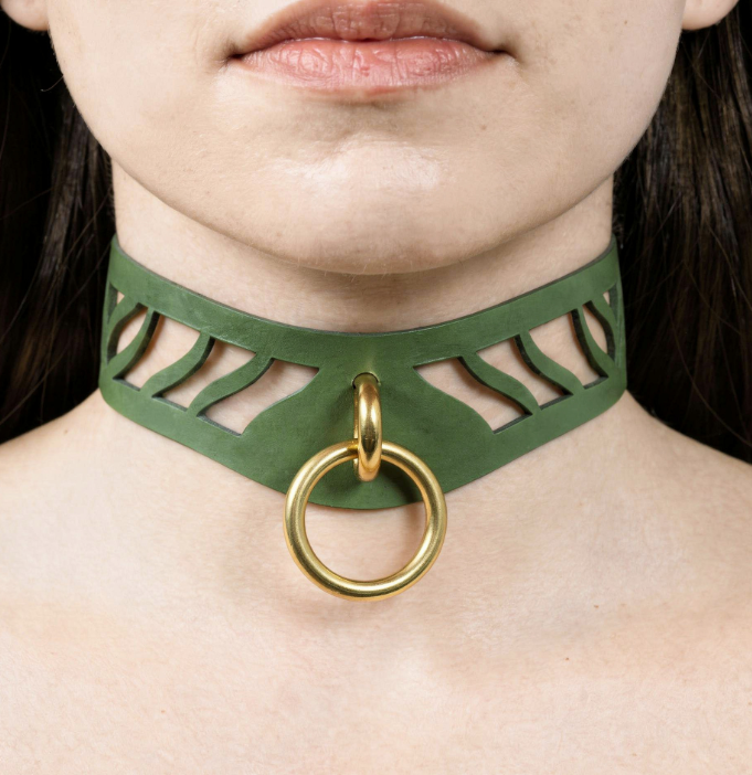 A close-up of a person's neck and chest area, featuring a green choker necklace with a gold ring and a cutout design.