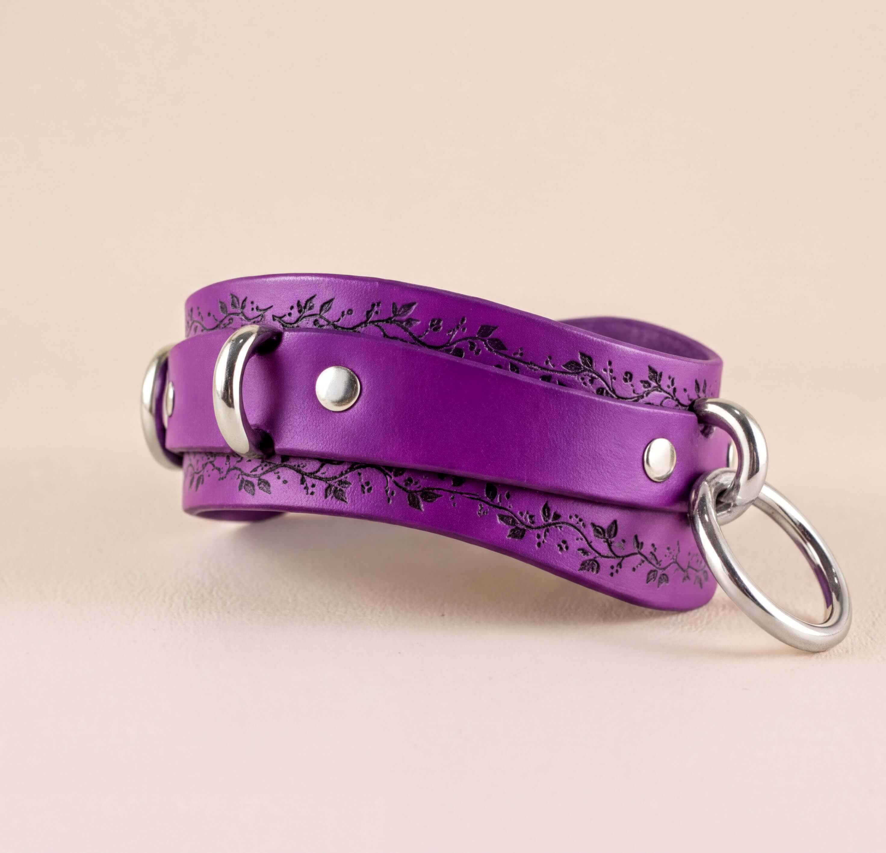 A purple leather collar with a floral design and metal rings on the ends.