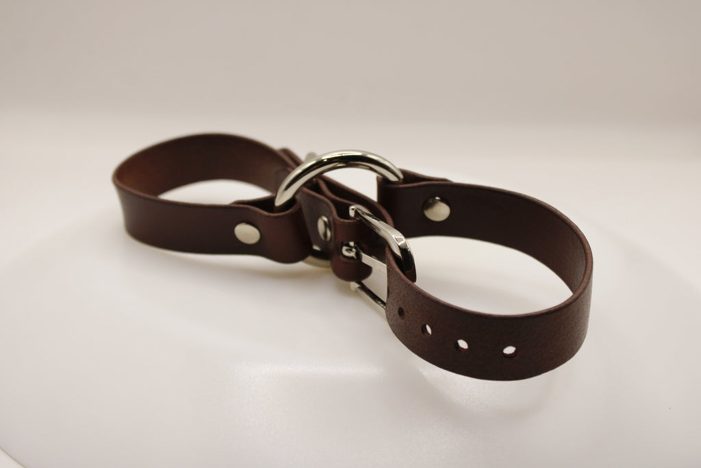 A brown leather strap with metal buckles and holes, resting on a white surface.