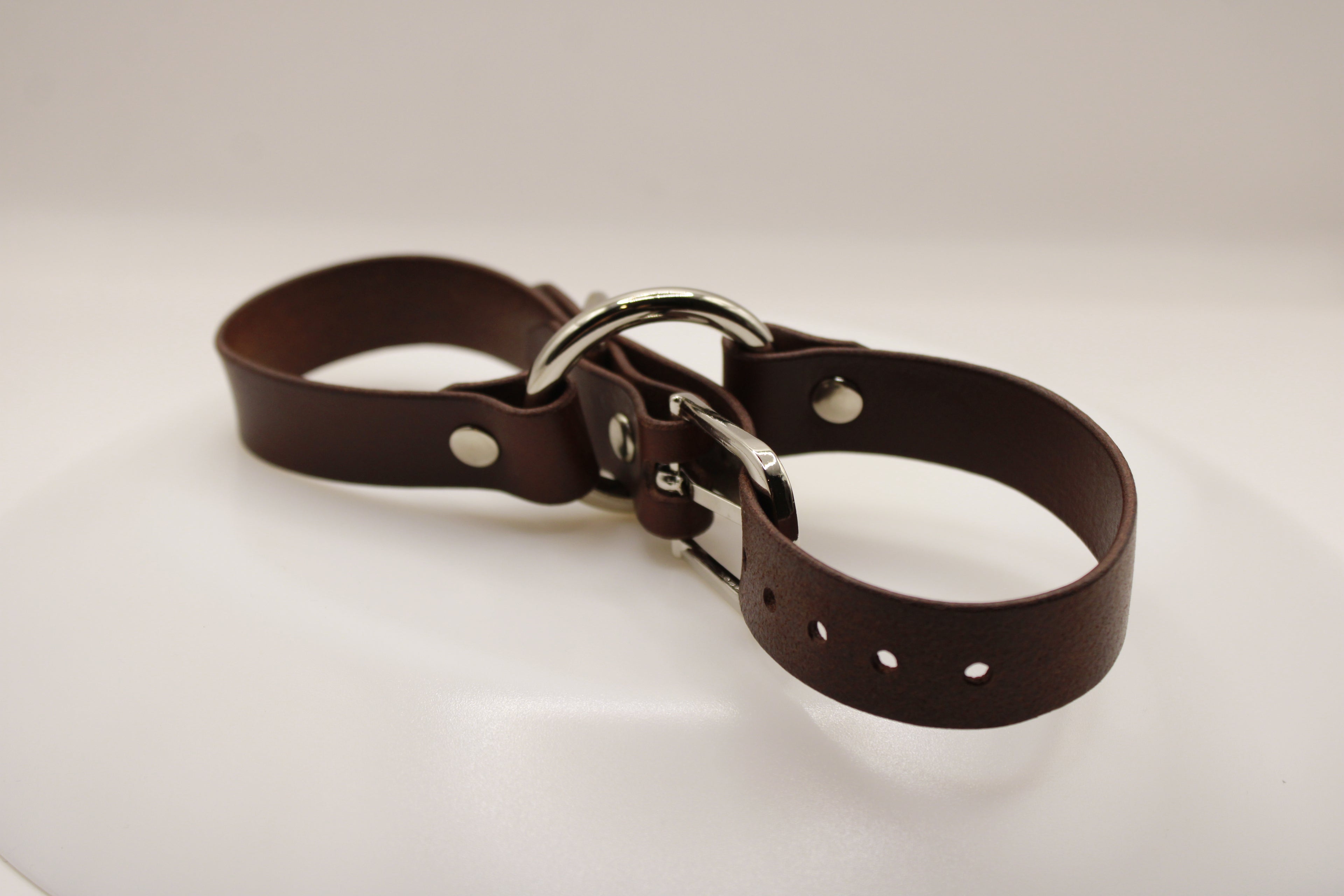 A brown leather strap with metal buckles and holes, resting on a white surface.