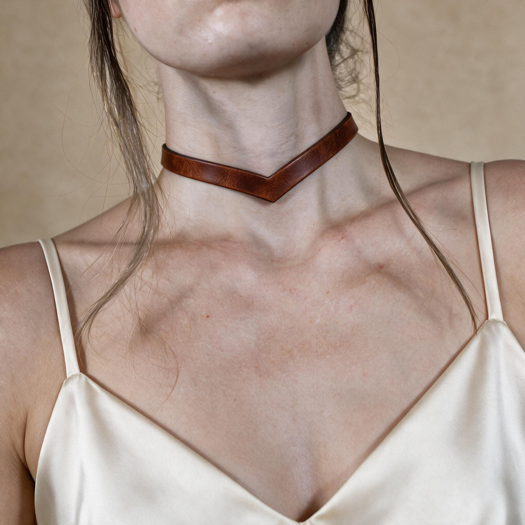 A close-up of a woman's neck and chest area wearing a brown leather choker necklace.