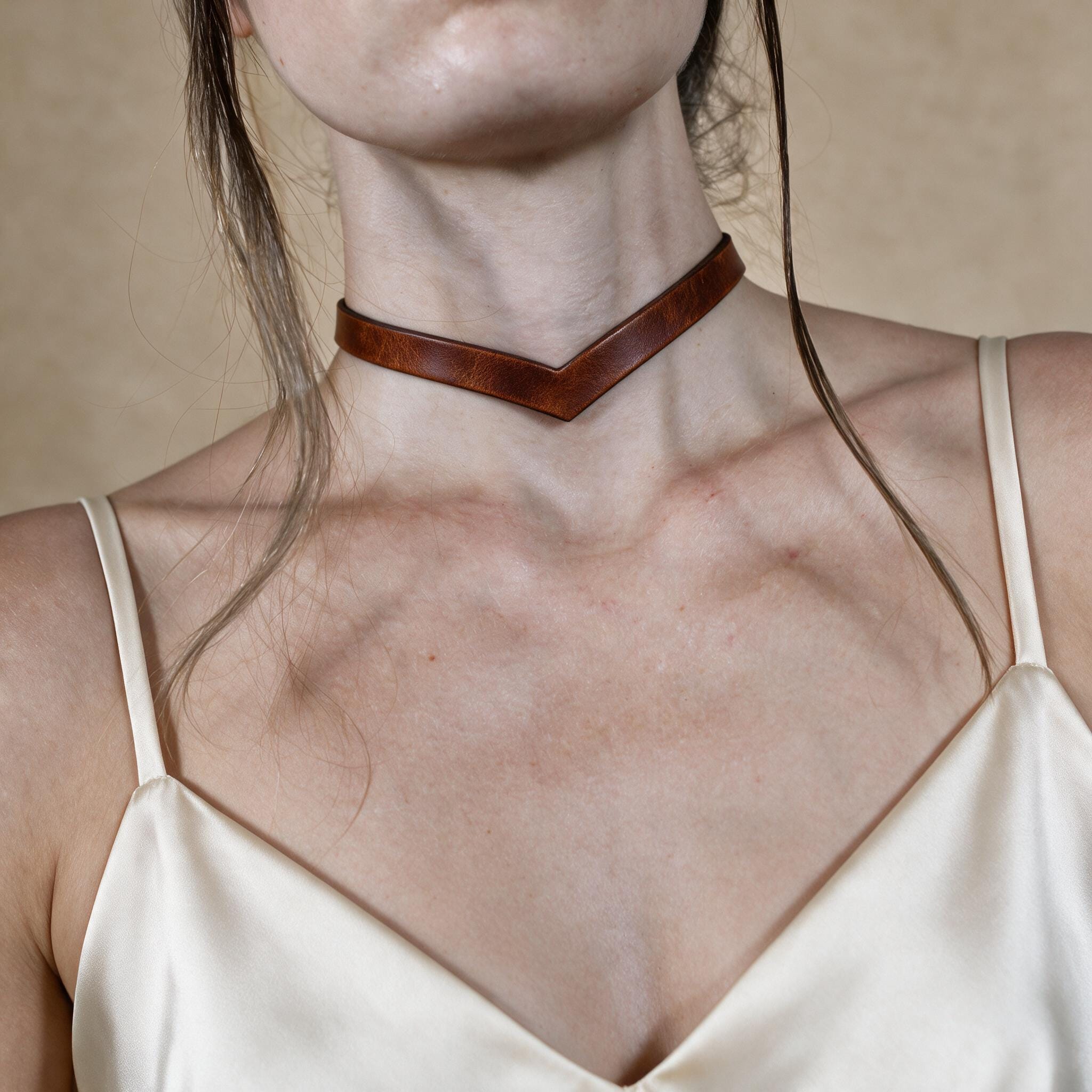 A close-up of a woman's neck and chest area wearing a brown leather choker necklace.