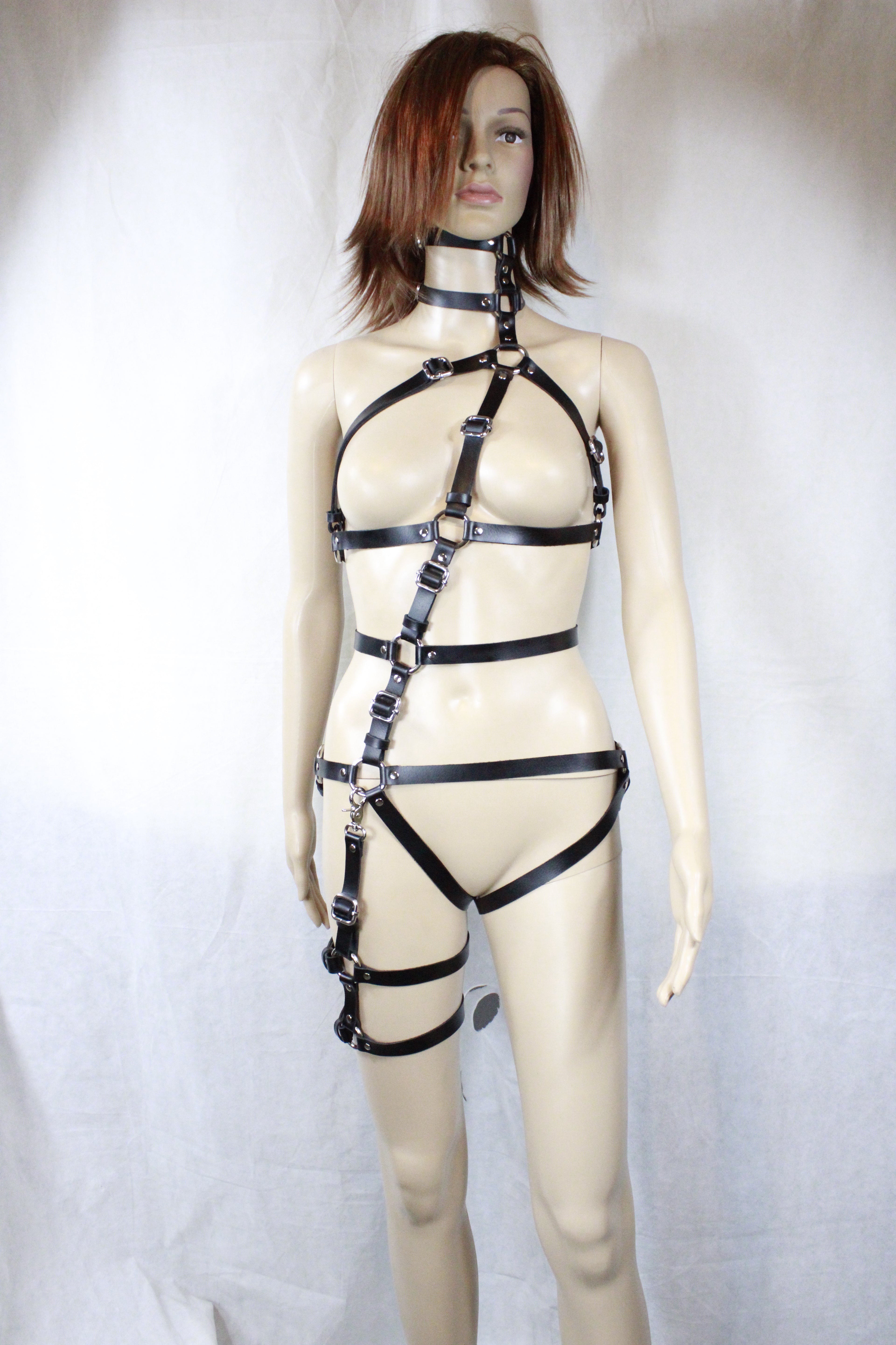 A mannequin wearing a strapless leather harness and straps, with its arms and legs spread out in a relaxed pose.
