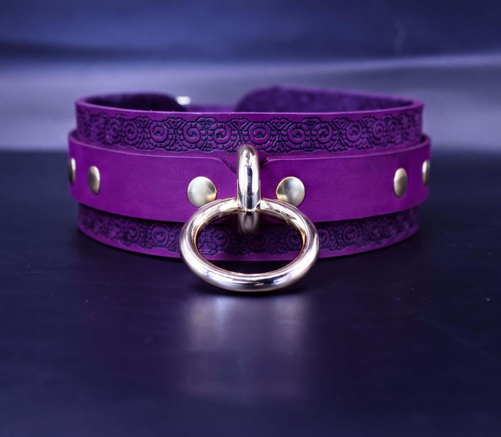 A purple leather choker necklace with a gold-colored metal ring and studs on the front.