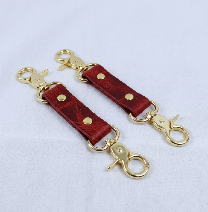 a pair of red leather straps with gold metal clasps and buckles, placed on a white surface.