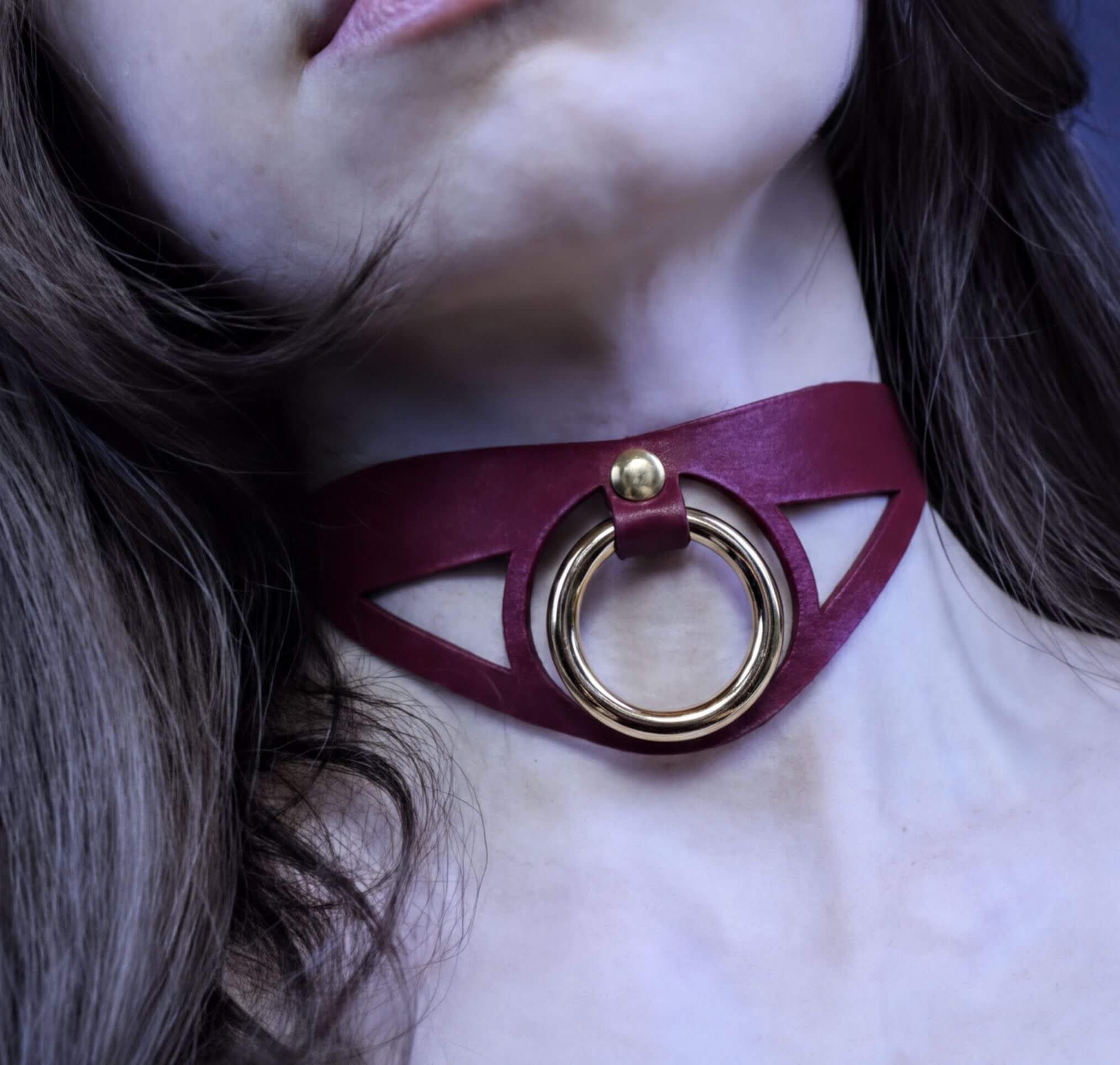 A close-up of a woman's neck with a burgundy choker necklace featuring a gold ring.