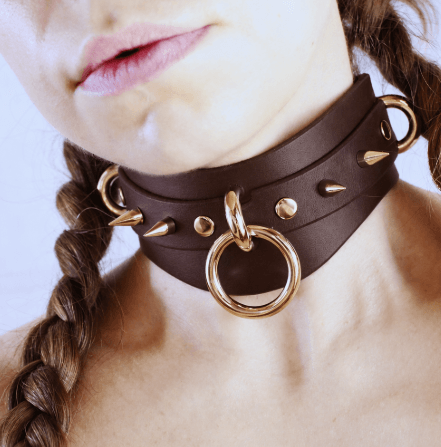 A close-up of a woman's neck with a large, ornate choker necklace featuring a gold ring and spikes.