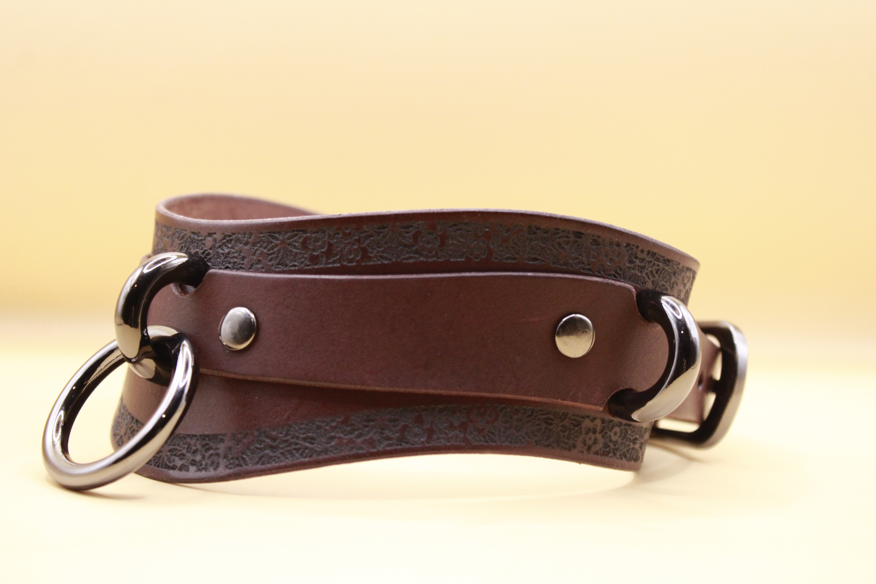 A brown leather choker necklace with metal rings and a decorative pattern on the leather.