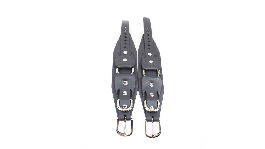 A pair of black leather straps with metal buckles and buckles, arranged side by side against a white background.