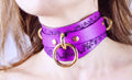 A close-up of a woman's neck wearing a purple choker necklace with a gold ring and floral design.