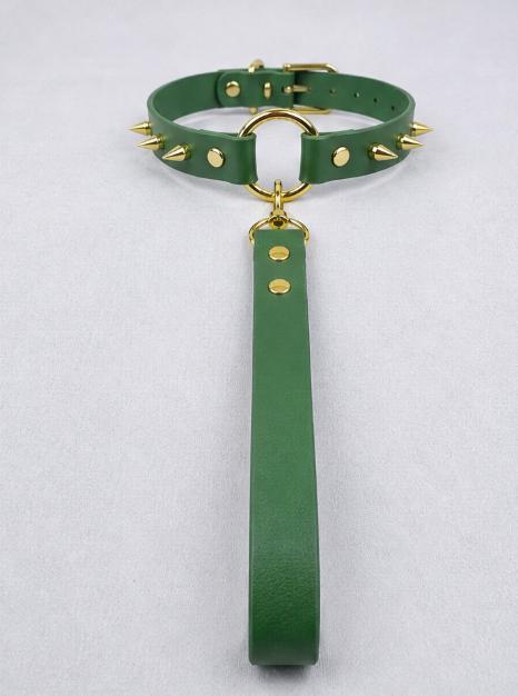 A green leather choker collar with spikes and a gold-colored metal ring is displayed on a white surface.