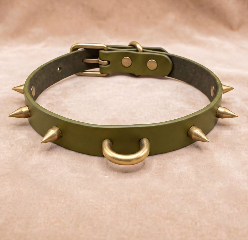 A green leather collar with spikes protruding from it, featuring two metal rings at the bottom.
