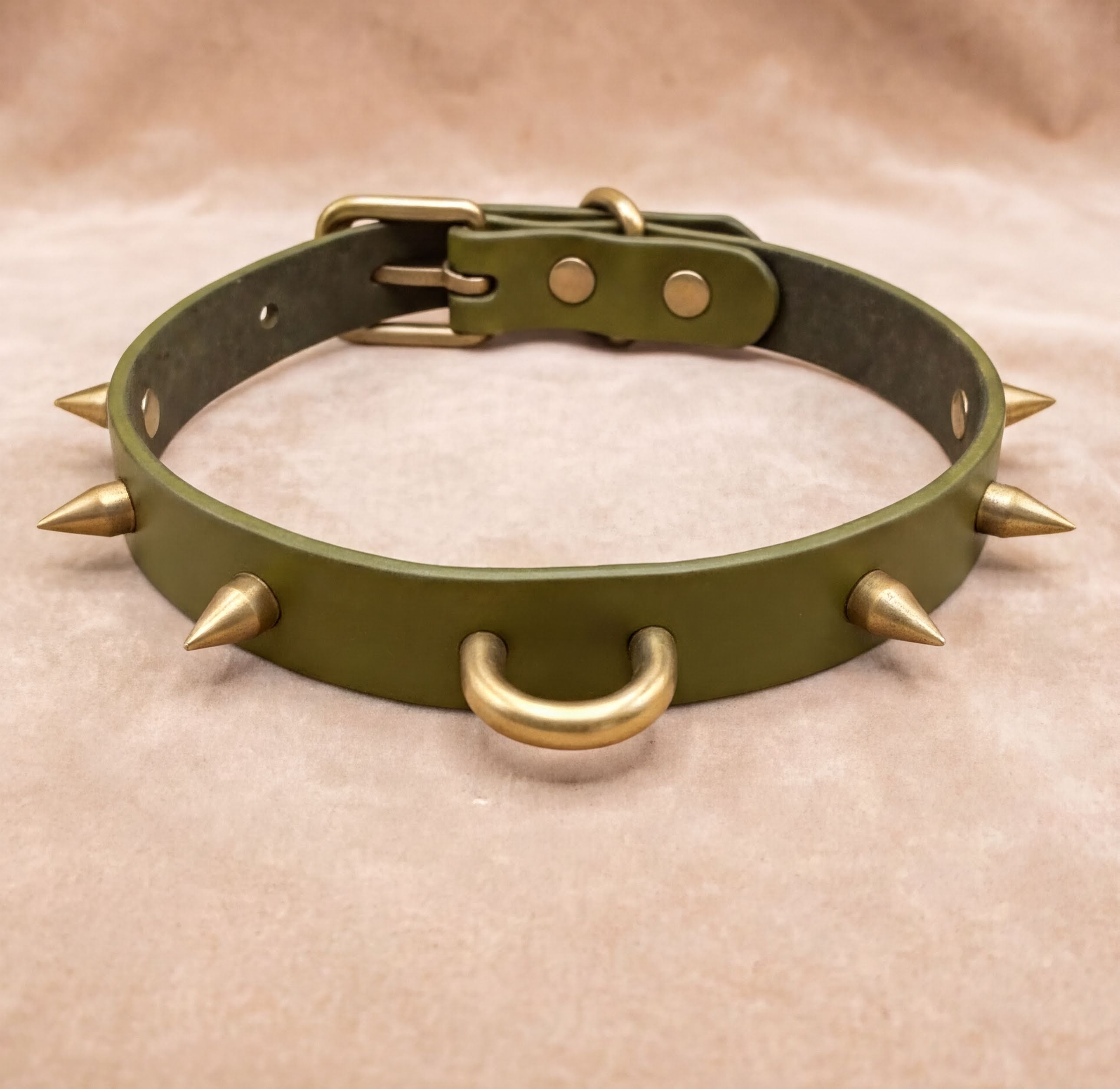 A green leather collar with spikes protruding from it, featuring two metal rings at the bottom.