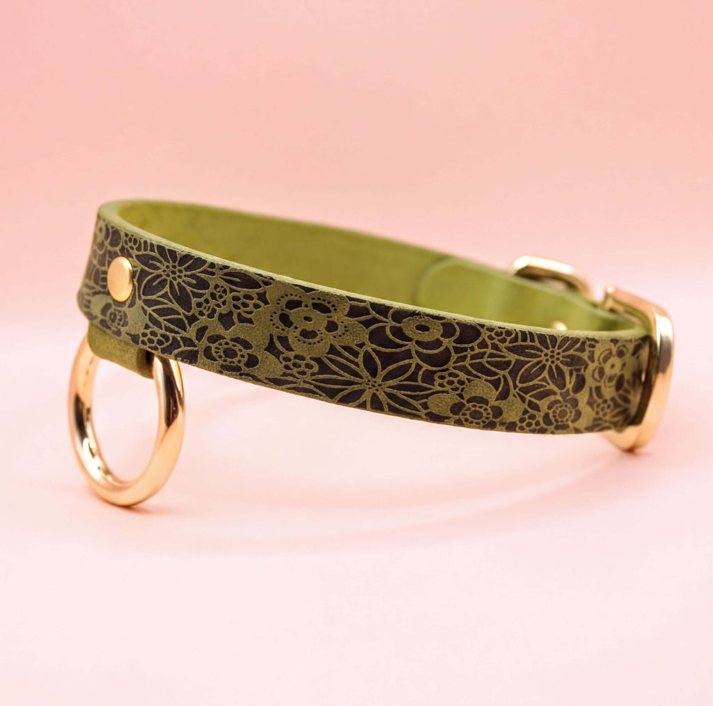A green leather collar with a floral pattern and two gold-colored rings on the sides.