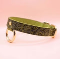 A green leather collar with a floral pattern and two gold-colored rings on the sides.