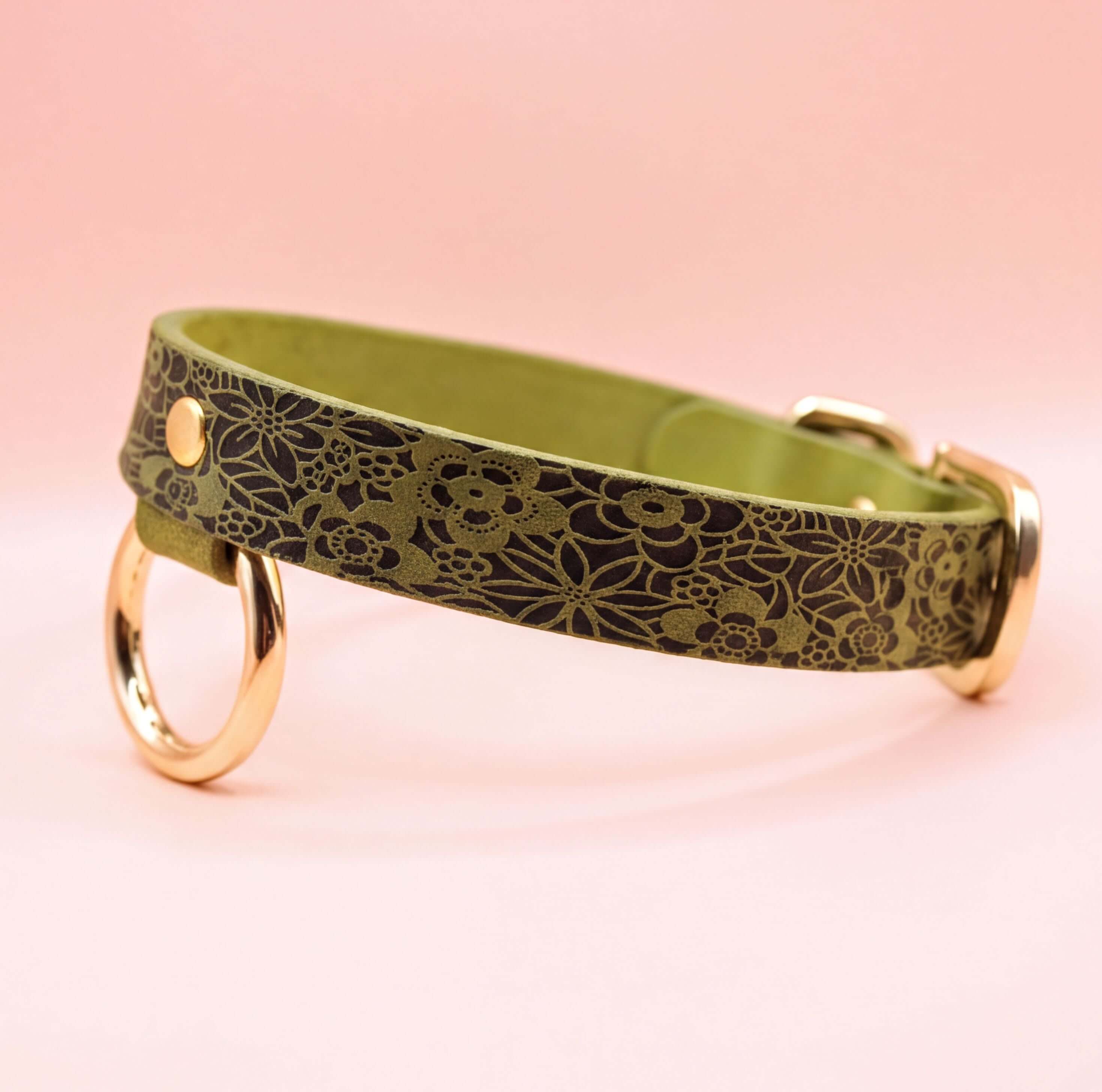 A green leather collar with a floral pattern and two gold-colored rings on the sides.