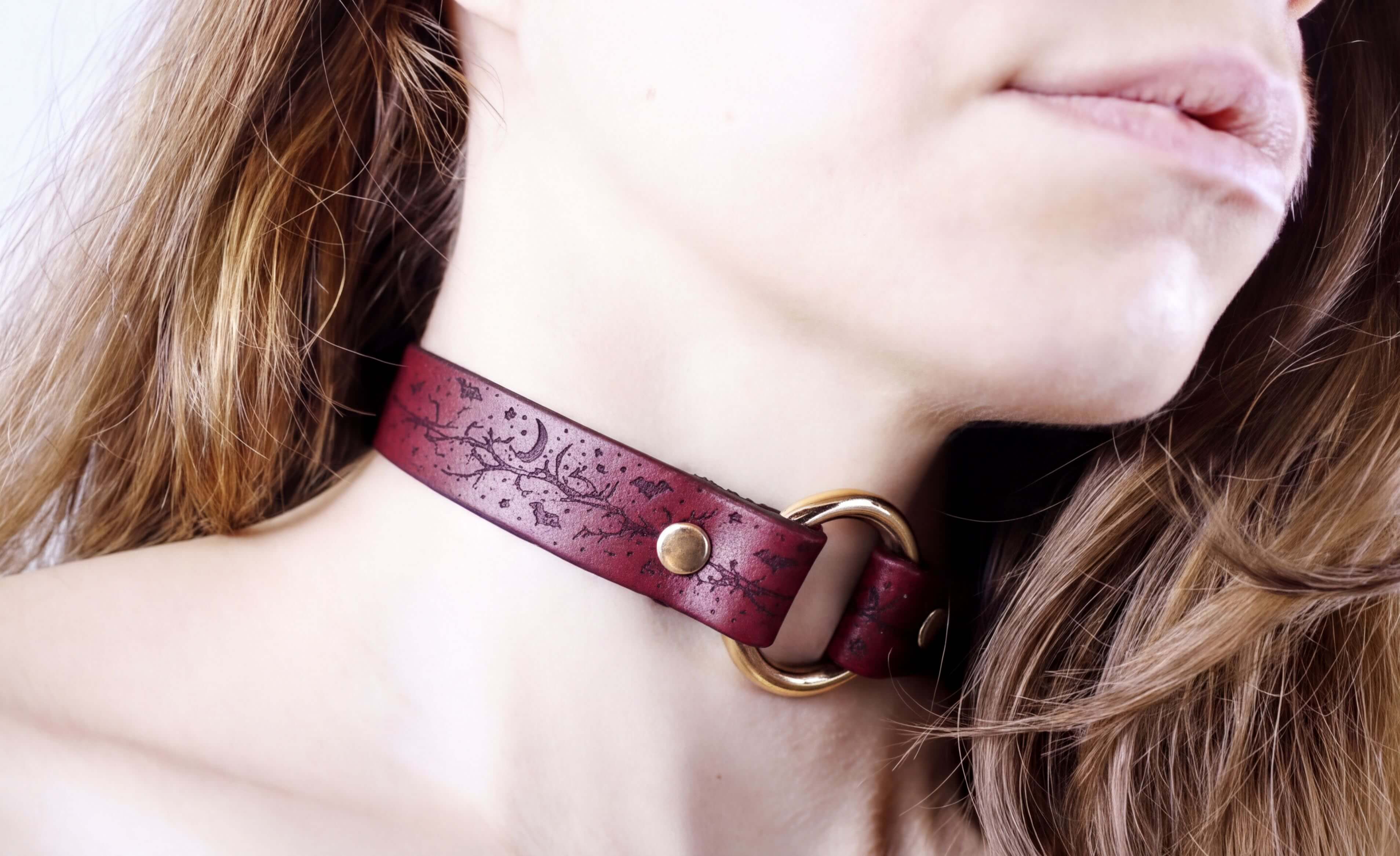 A close-up of a person's neck and chin wearing a burgundy leather choker necklace with a gold-colored buckle.