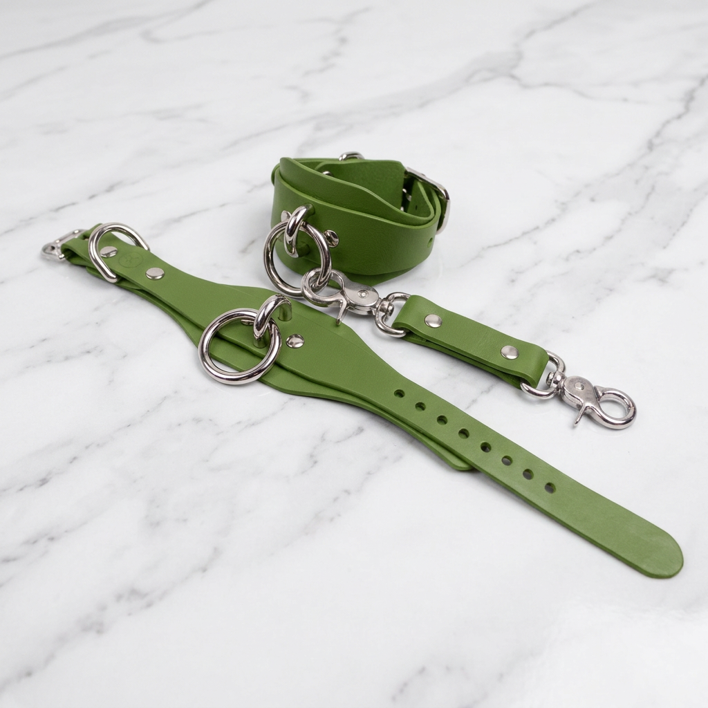 a pair of green leather straps with metal rings and buckles, resting on a marble surface.