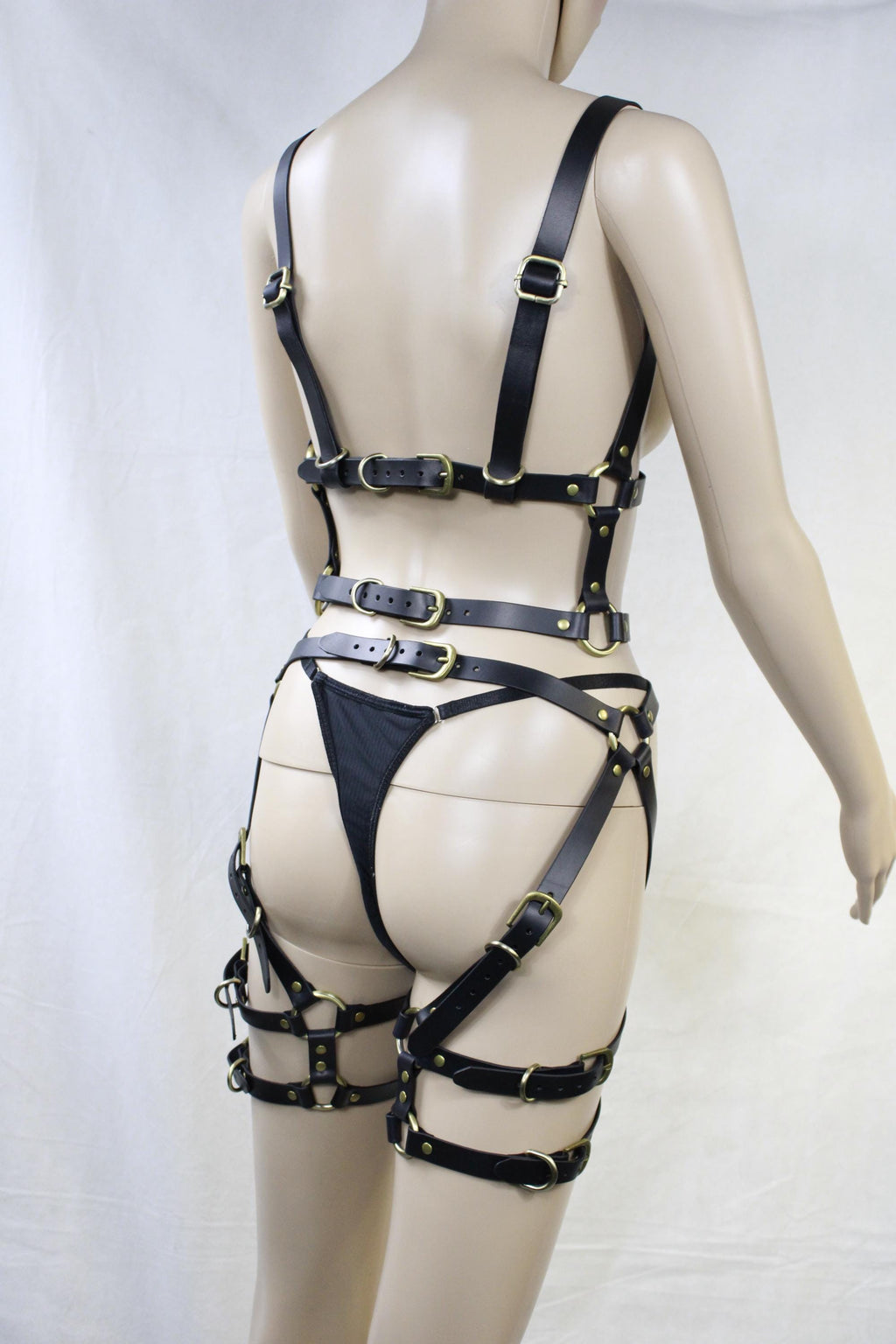 A mannequin wearing a leather strap ensemble, including straps, buckles, and a bra-like garment.