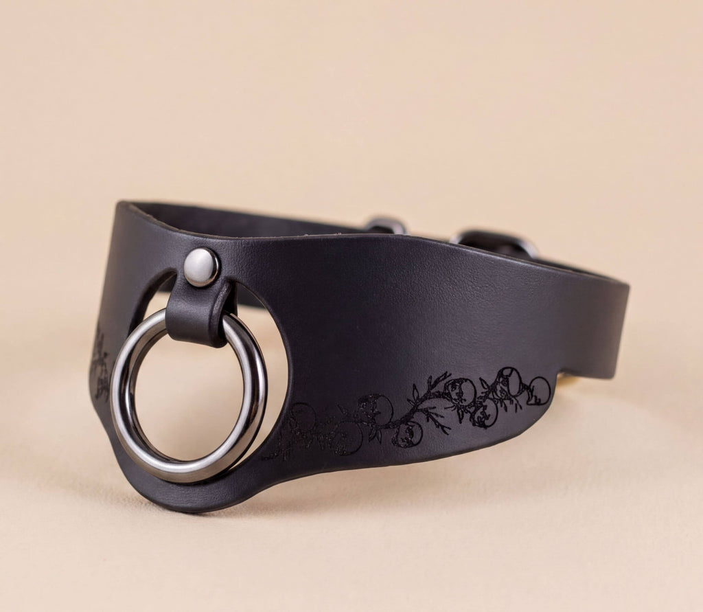 A black leather choker necklace with a metal ring and floral design on the side.