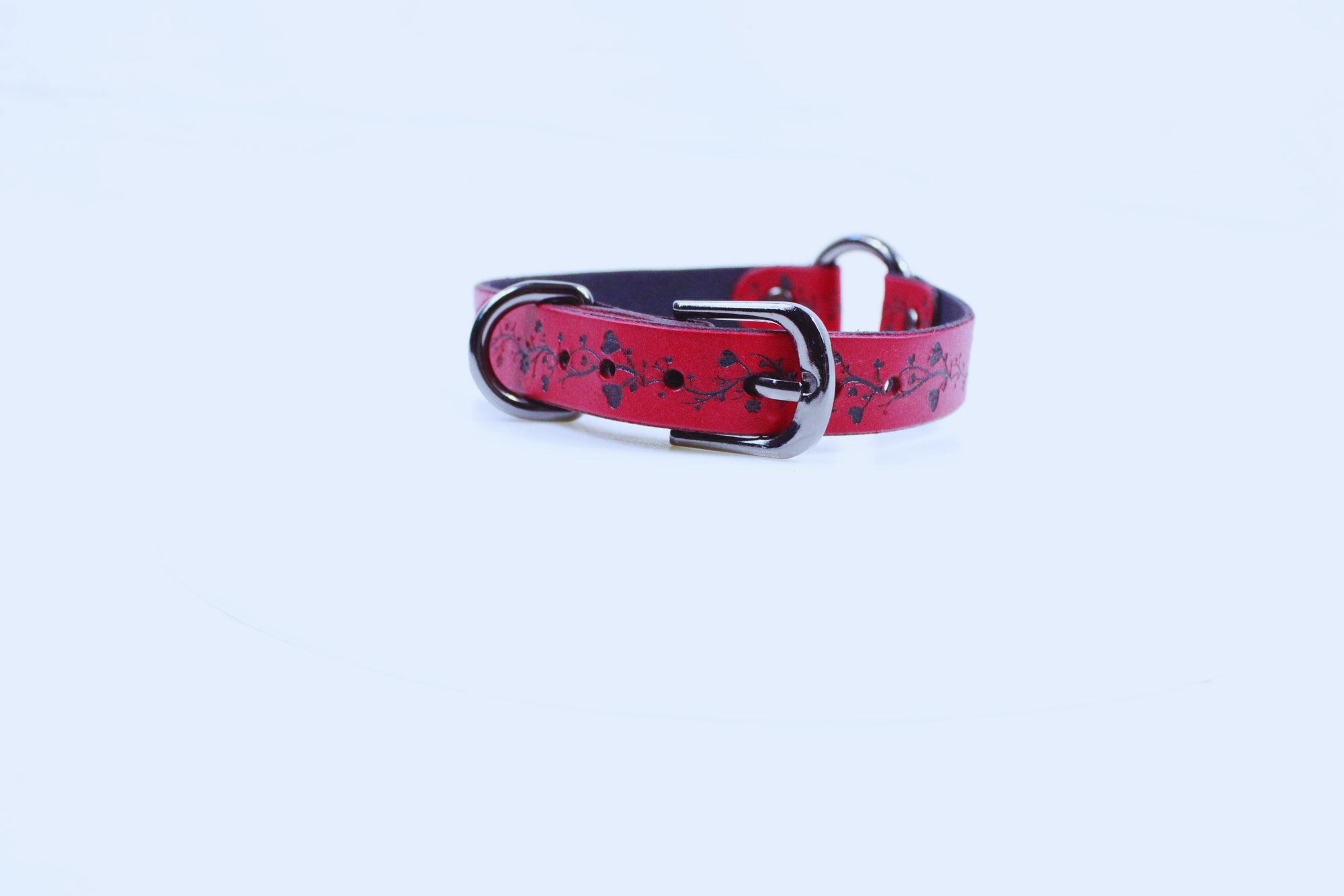 A red leather dog collar with a metal buckle and decorative pattern on the surface.