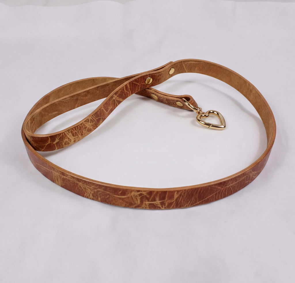 A brown leather leash with a gold-colored metal clasp and a heart-shaped charm attached.