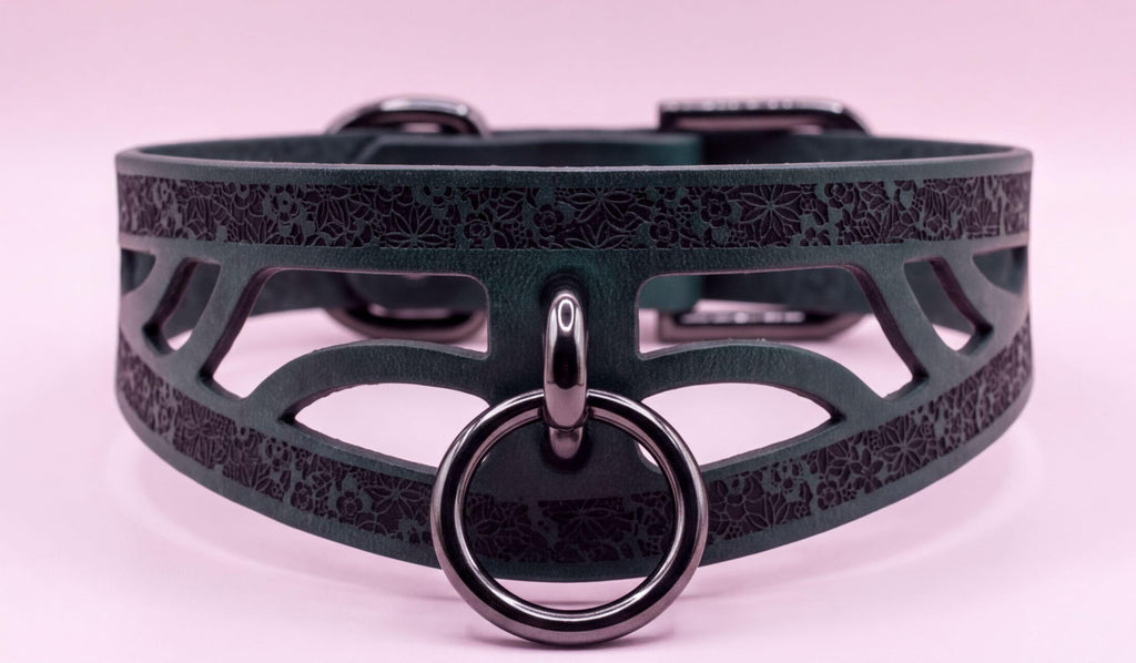 A close-up image of a dark green choker necklace with a metal ring and a decorative pattern on the front.