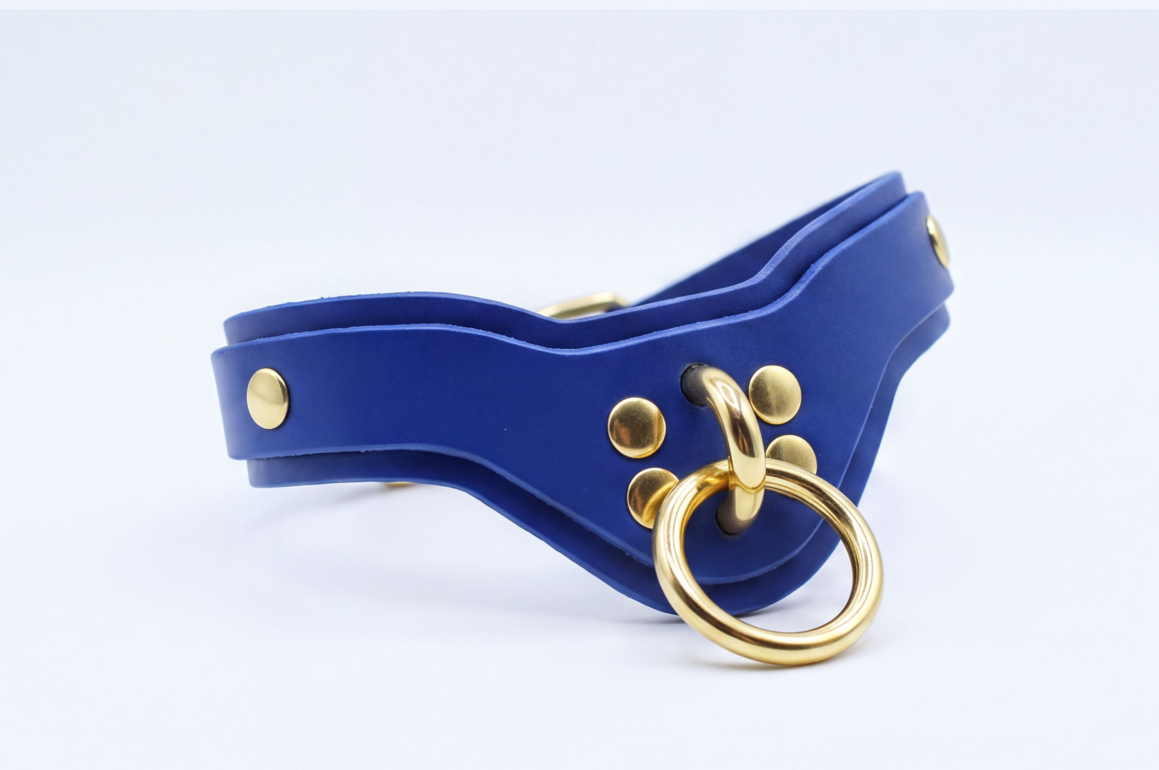 A blue leather collar with a gold ring and studs, featuring a curved shape and a metallic appearance.