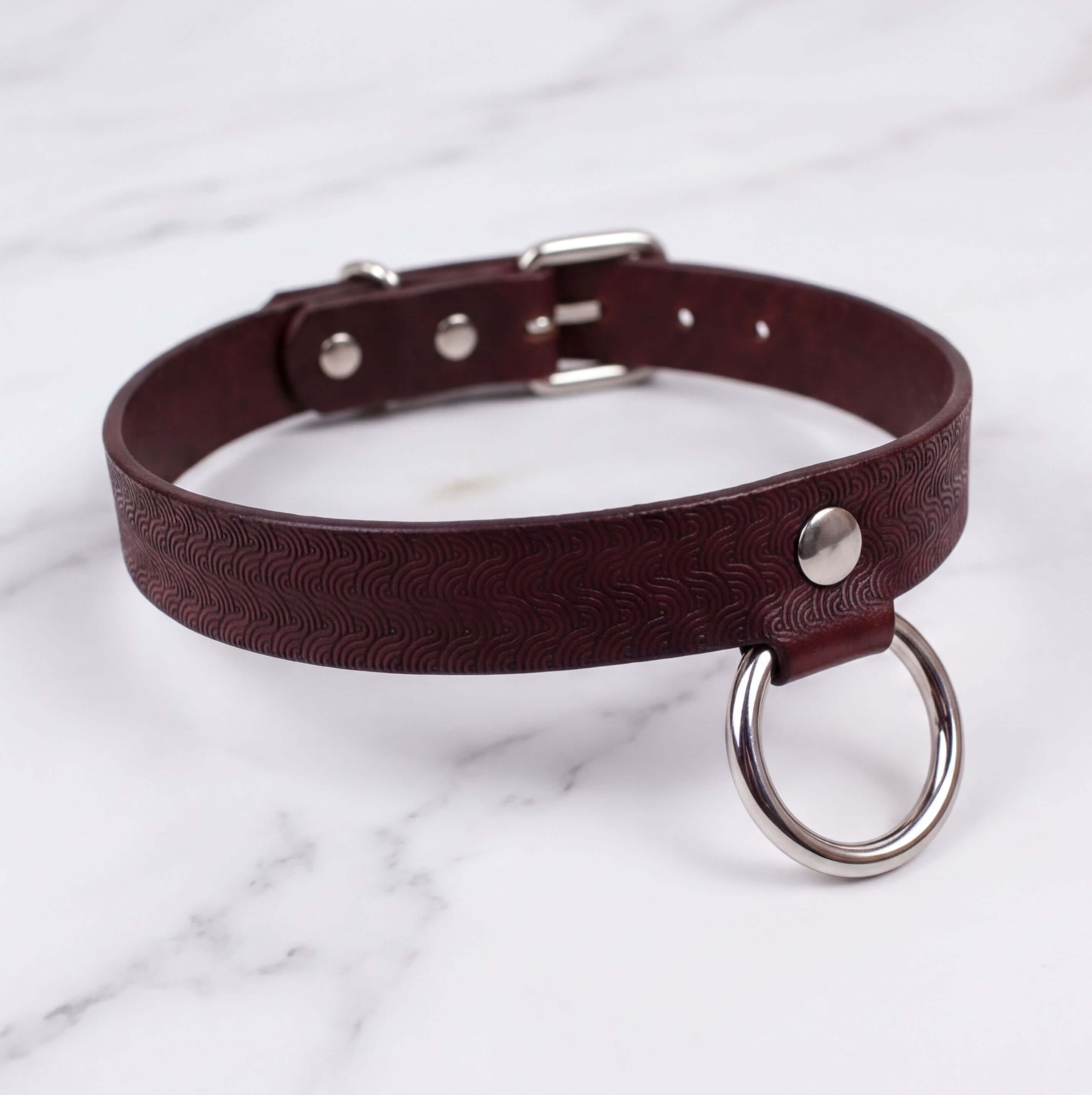 A brown leather choker collar with a metal ring and buckle.