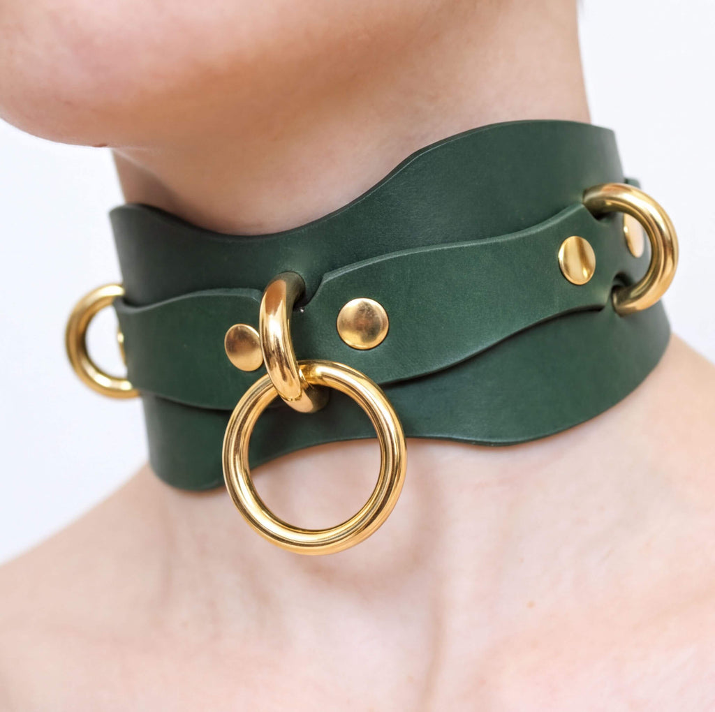 A close-up of a person's neck wearing a green leather choker necklace with gold-colored metal rings.