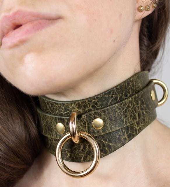A close-up of a woman's neck and chin wearing a dark green leather choker necklace with gold-colored metal rings.