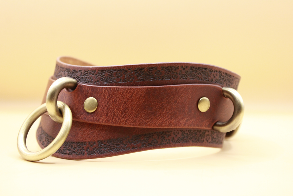 A brown leather strap with metal rings and buckles, resting on a plain background.