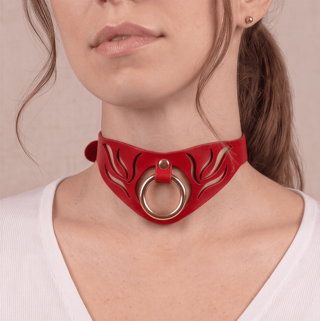 A close-up of a woman's neck and chin wearing a red choker necklace with a gold ring.